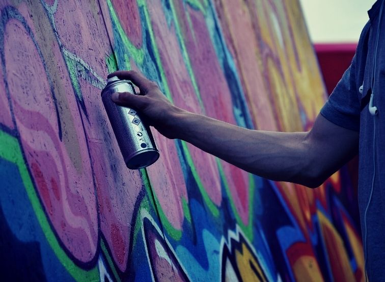 Männliche Person sprüht ein Graffiti an die Wand