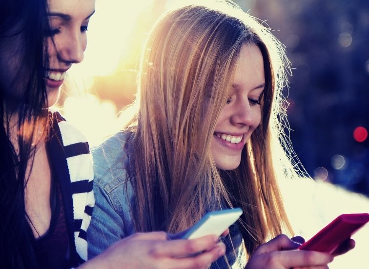 Zwei junge Frauen schauen lächelnd auf ihre Smartphones